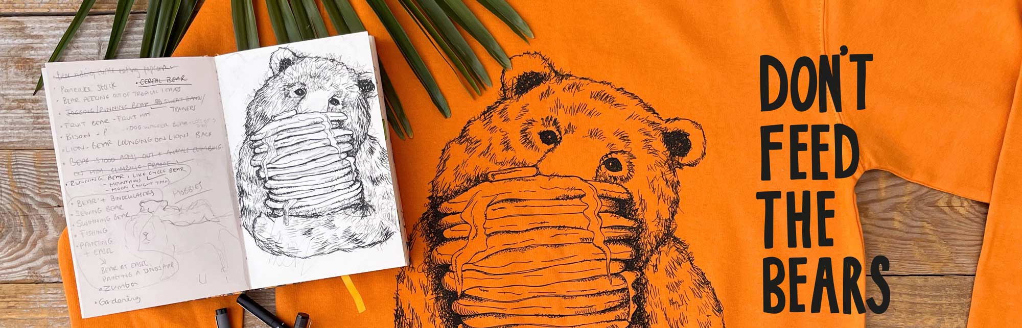 home page banner featuring bear jumper with illustration of a bear hiding behind a stack of pancakes. Next to it is the origional sketch book idea drwan in pencil and fine liner. 