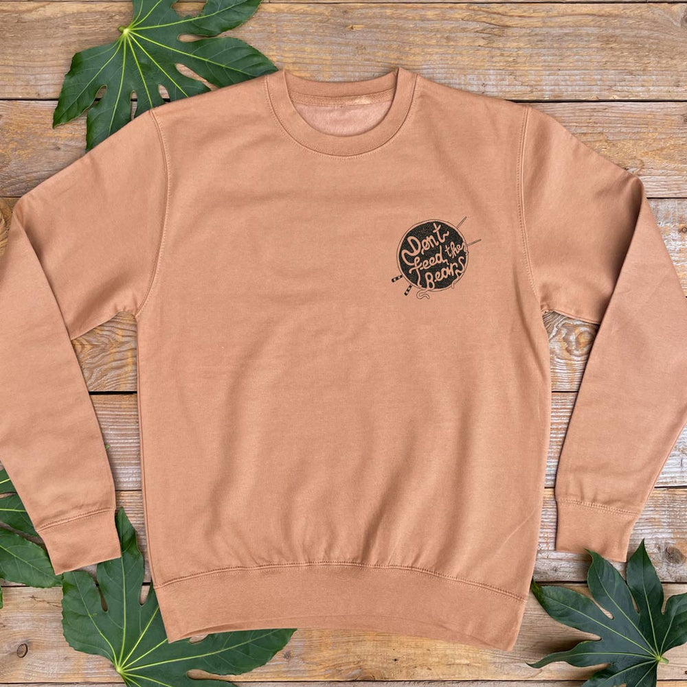 Brown sweatshirt with a small graphic on a wooden surface with leaves