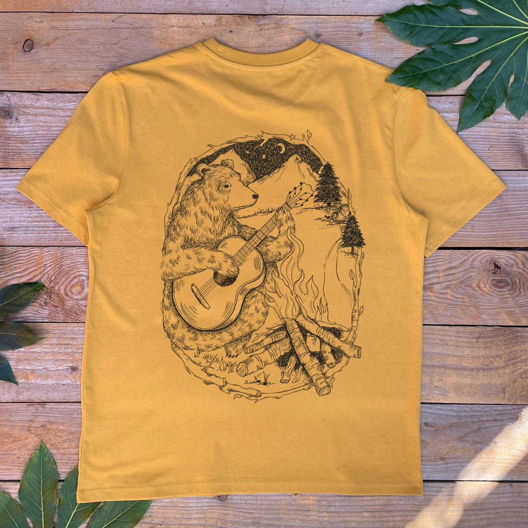 Yellow t-shirt with a bear playing guitar graphic on a wooden surface with leaves.